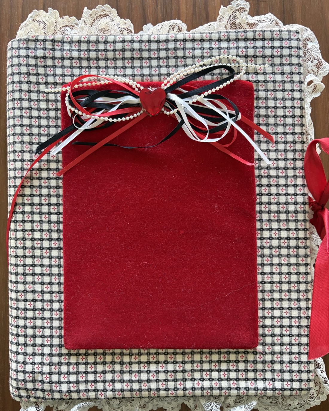 A handmade baby album covered in checked fabric and lace, with a red velvet panel and ribbons.