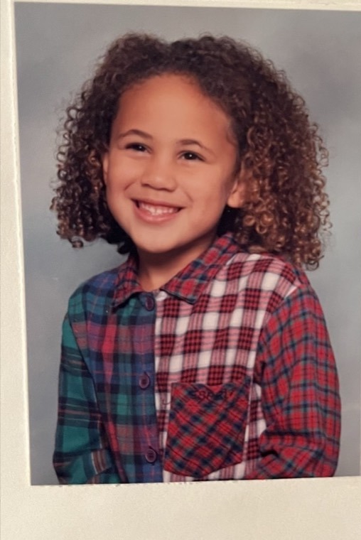 Alexis as a child in a school portrait, wearing a plaid shirt.