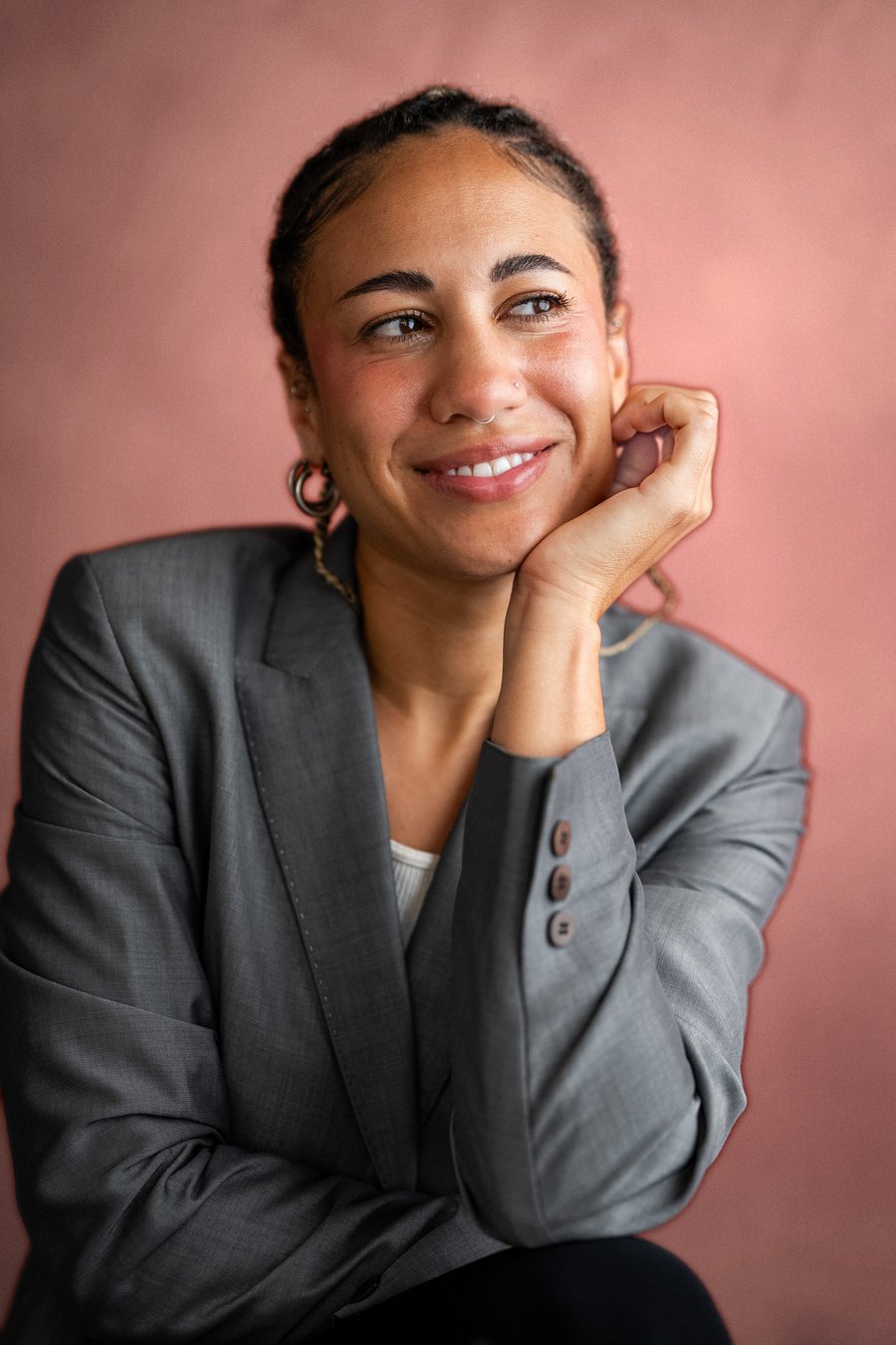 Alexis Kimball smiling, wearing a grey blazer, hand resting under her chin, against a soft muted backdrop.
